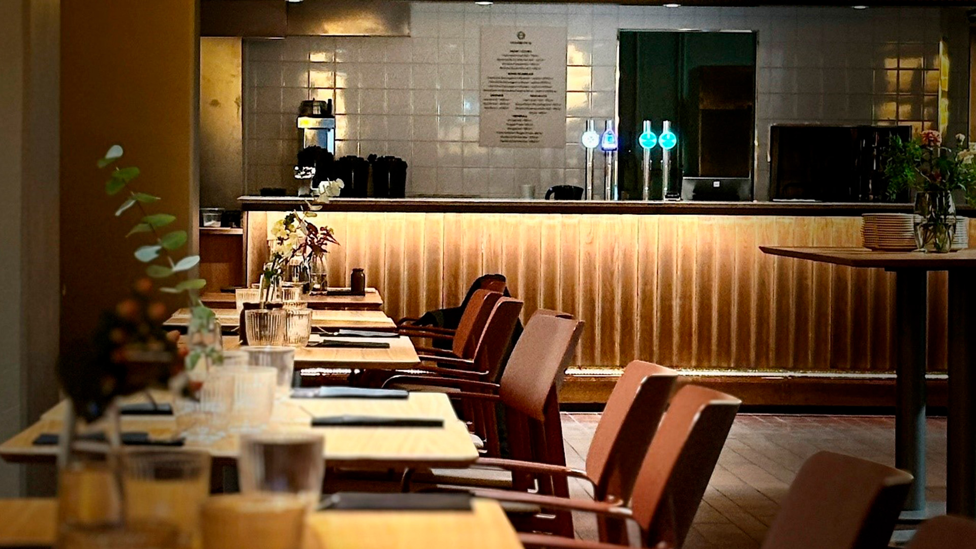 Restaurang med dämpad belysning. Bord och stolar i rad mot väggen och en bardisk.